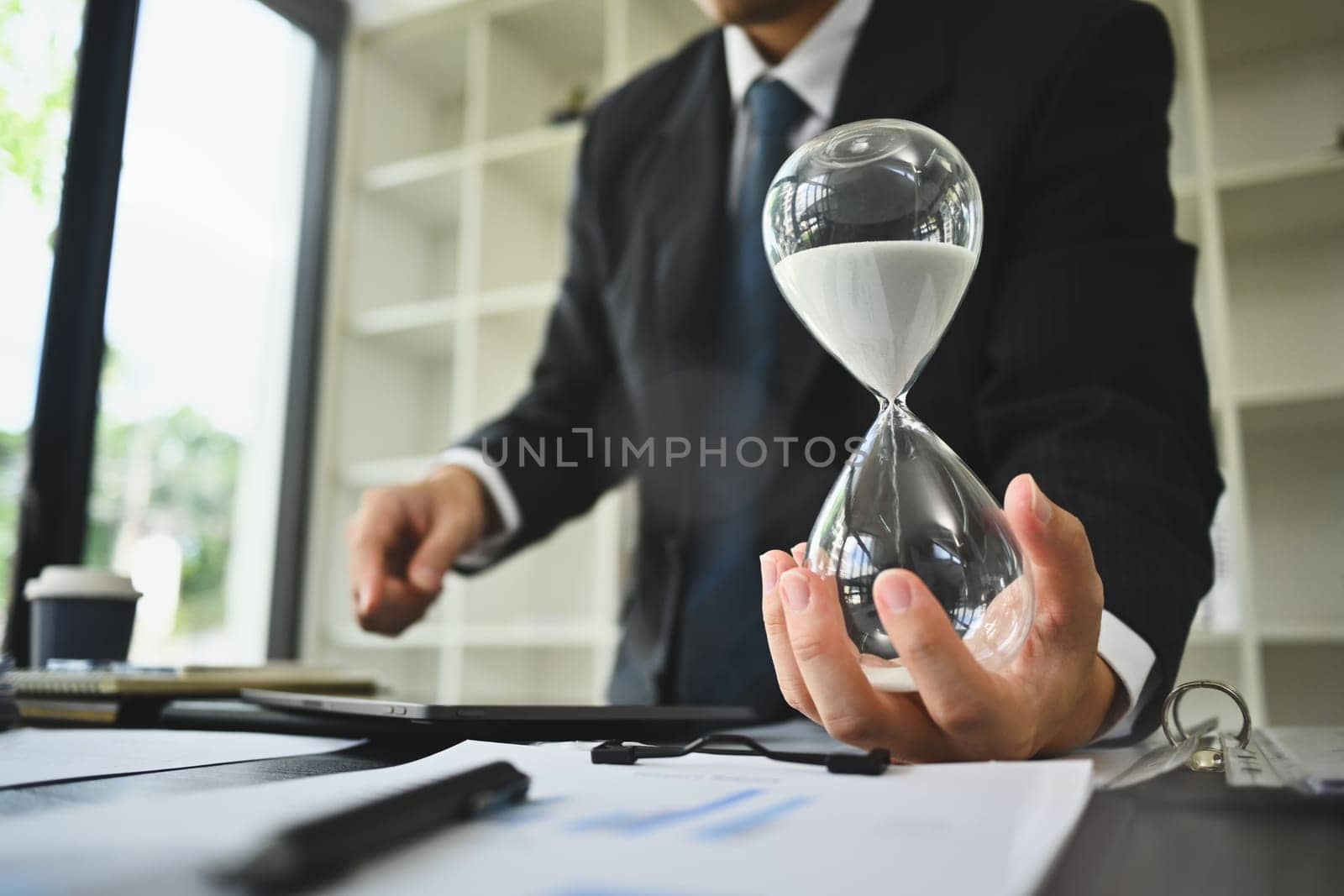 Hand of businessman holding hourglass. Business and time management concept by prathanchorruangsak