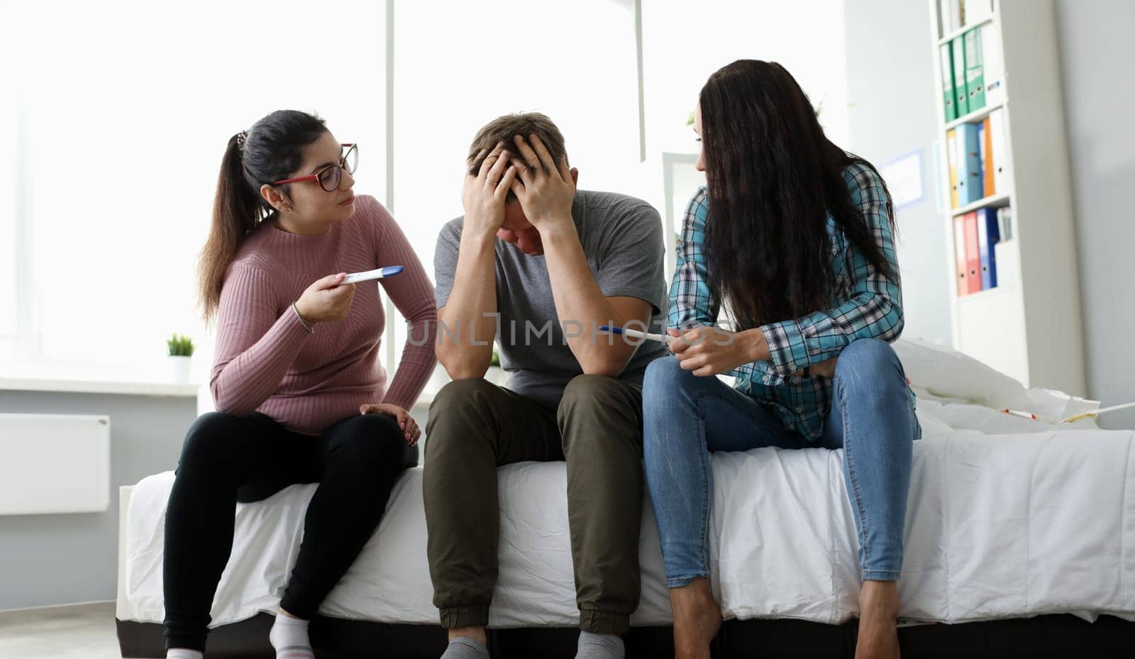 Boyfriend surrounded by girlfriends showing positive pregnancy tests. Angry females waiting babies from one male. Shocked and desperate boy holding his head