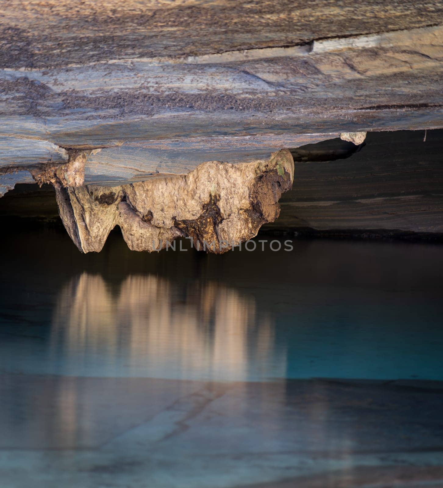 A huge stalactite reflects in a clear lagoon inside a brightly lit ancient cave, providing space for text