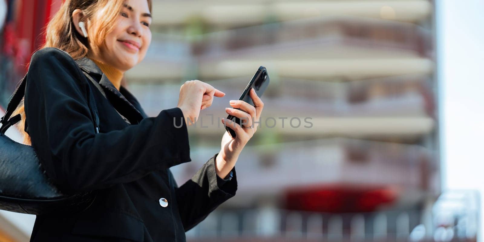 Asian professional businesswoman holding cellphone using smartphone standing or walking on big city urban street outside. Successful Asian business woman by nateemee