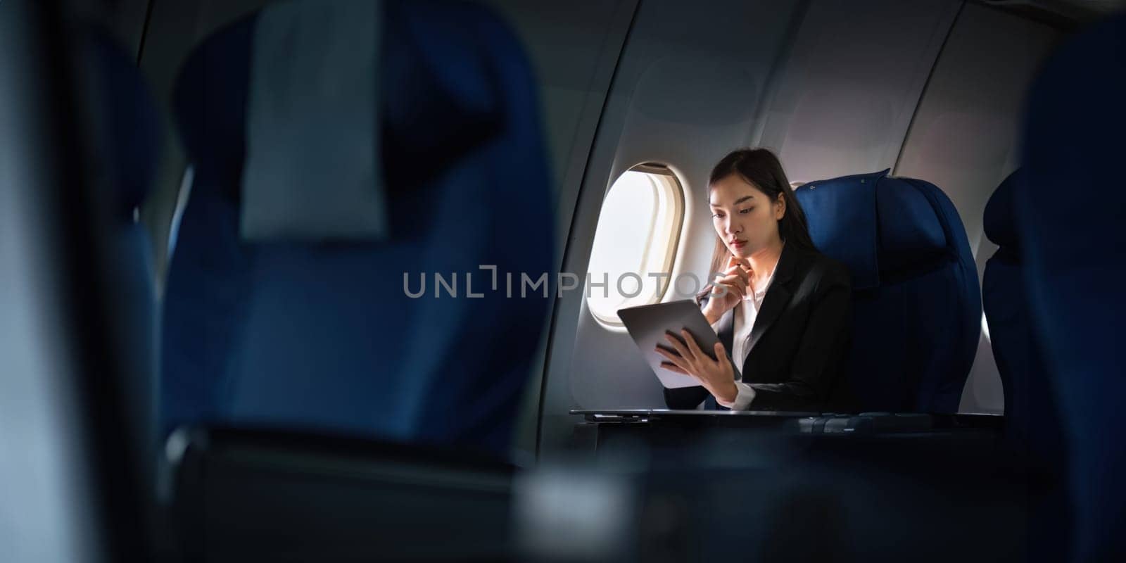 Successful Asian business woman, Business woman working in airplane cabin during flight on tablet.