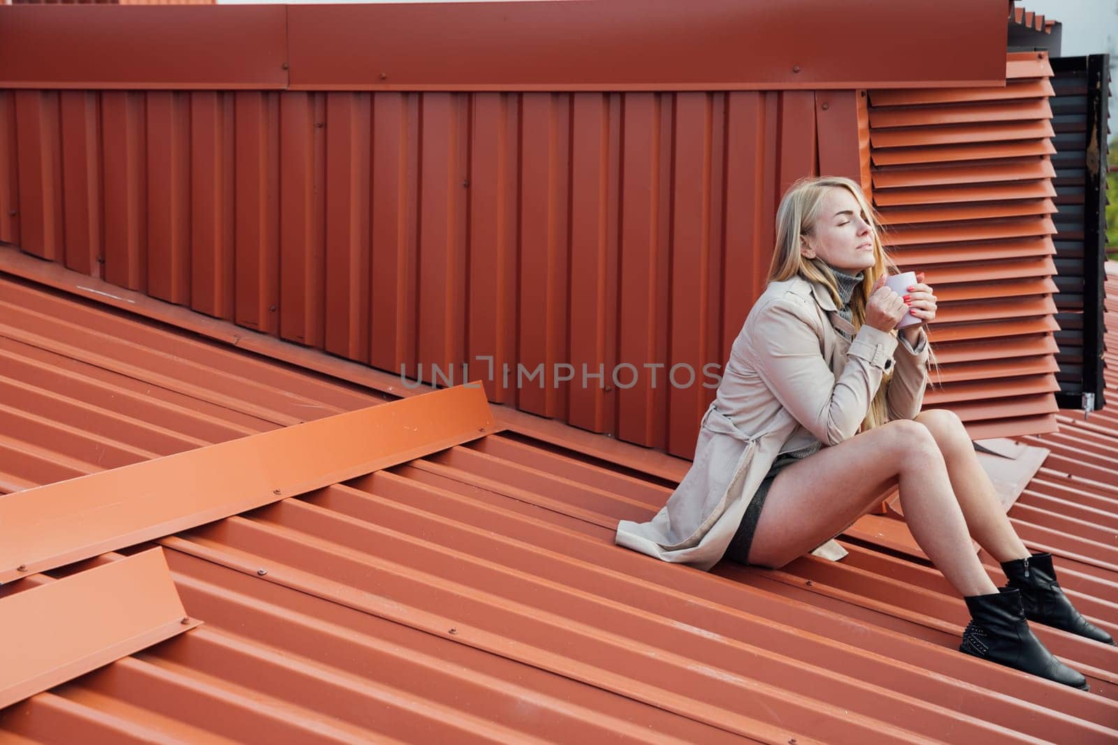 blonde beautiful woman with a cup of coffee on the roof of house on the street