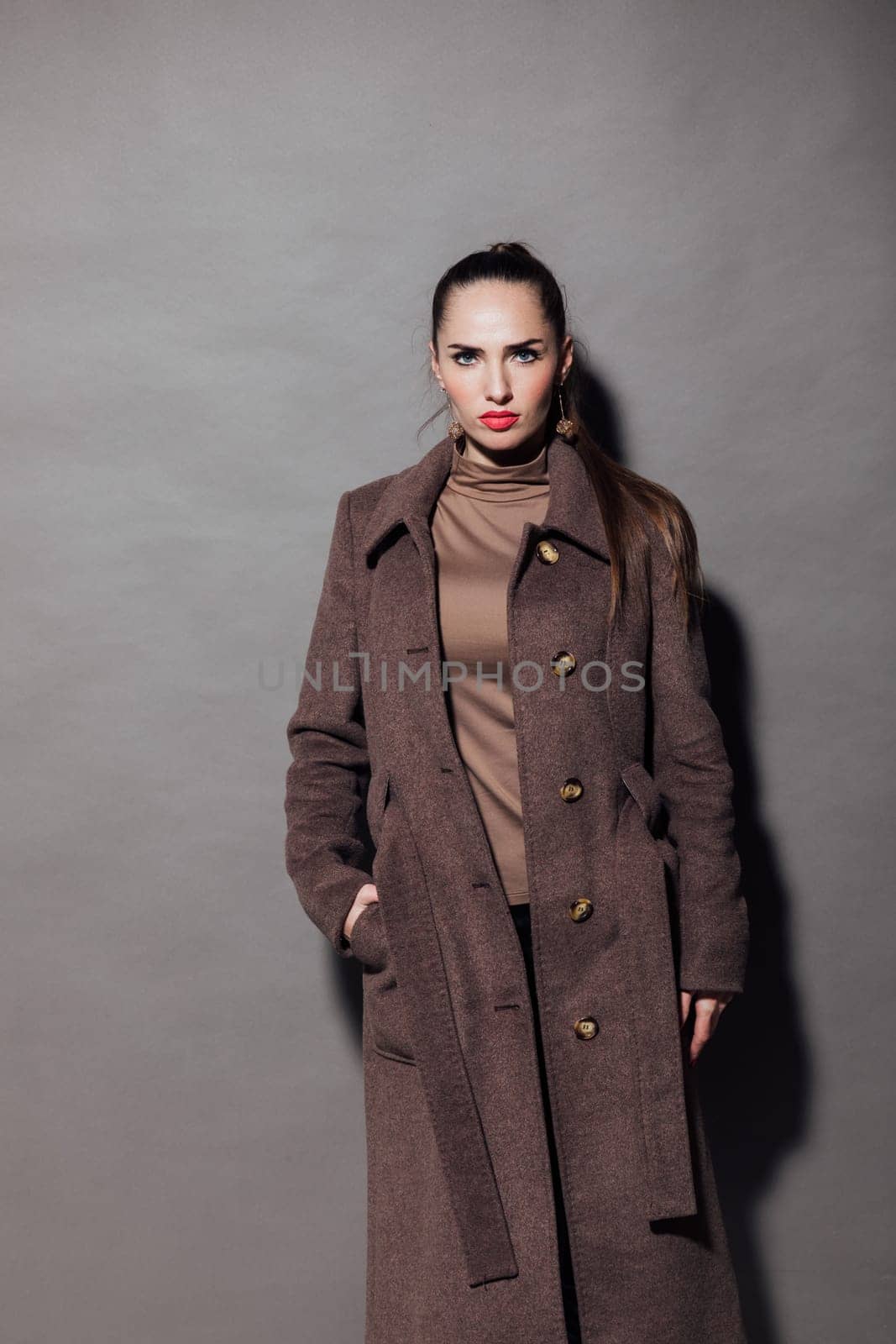 fashionable and beautiful woman in a brown cape stands on a gray background