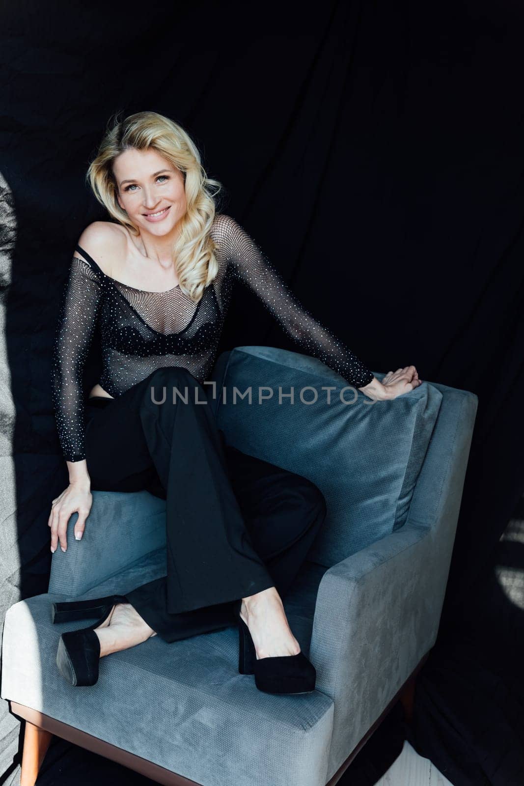 a beautiful blonde in black fashionable clothes on a black background in a chair