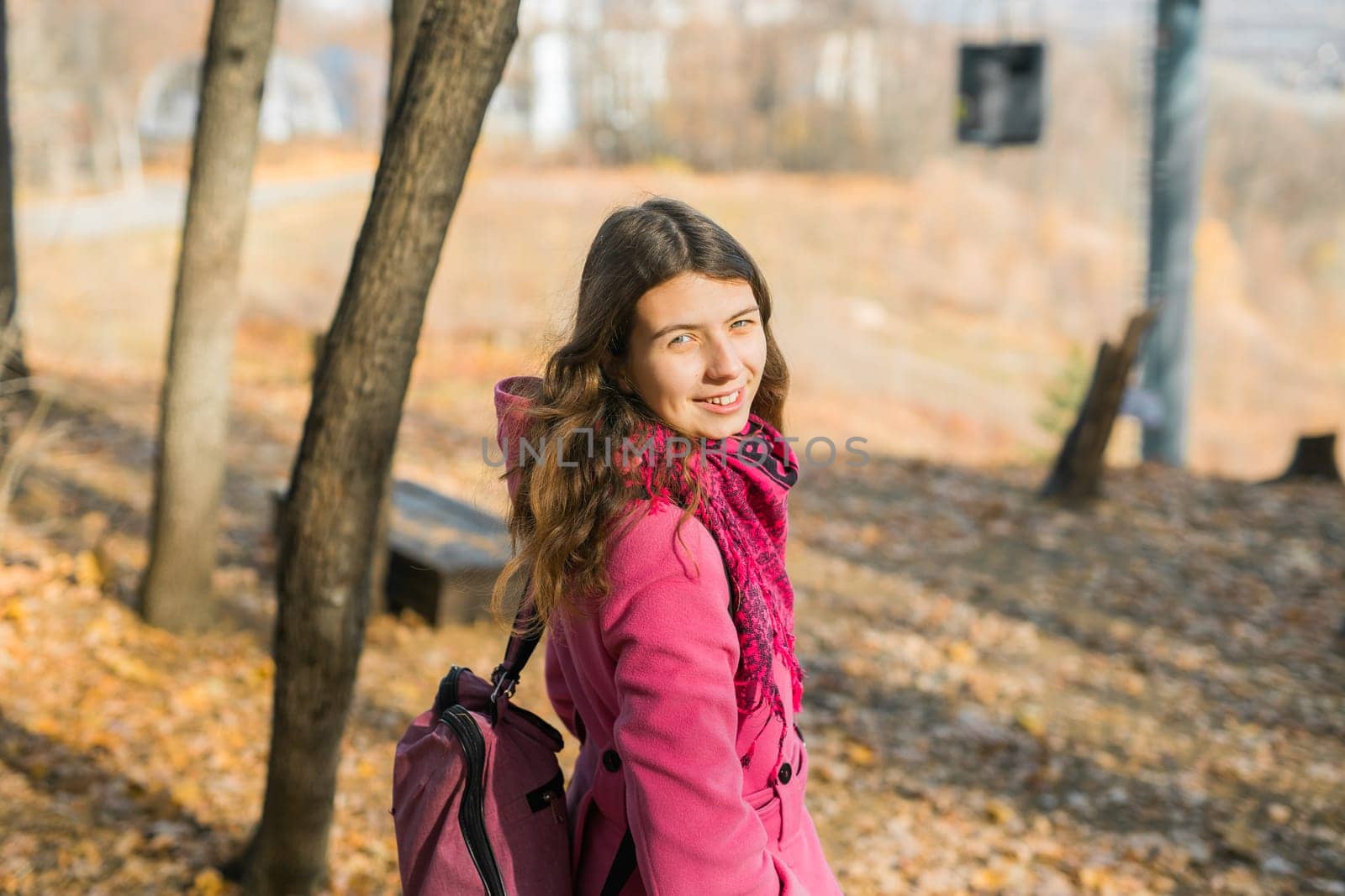 Back view of a girl walking on autumn park in fall season. Millennial generation and youth.