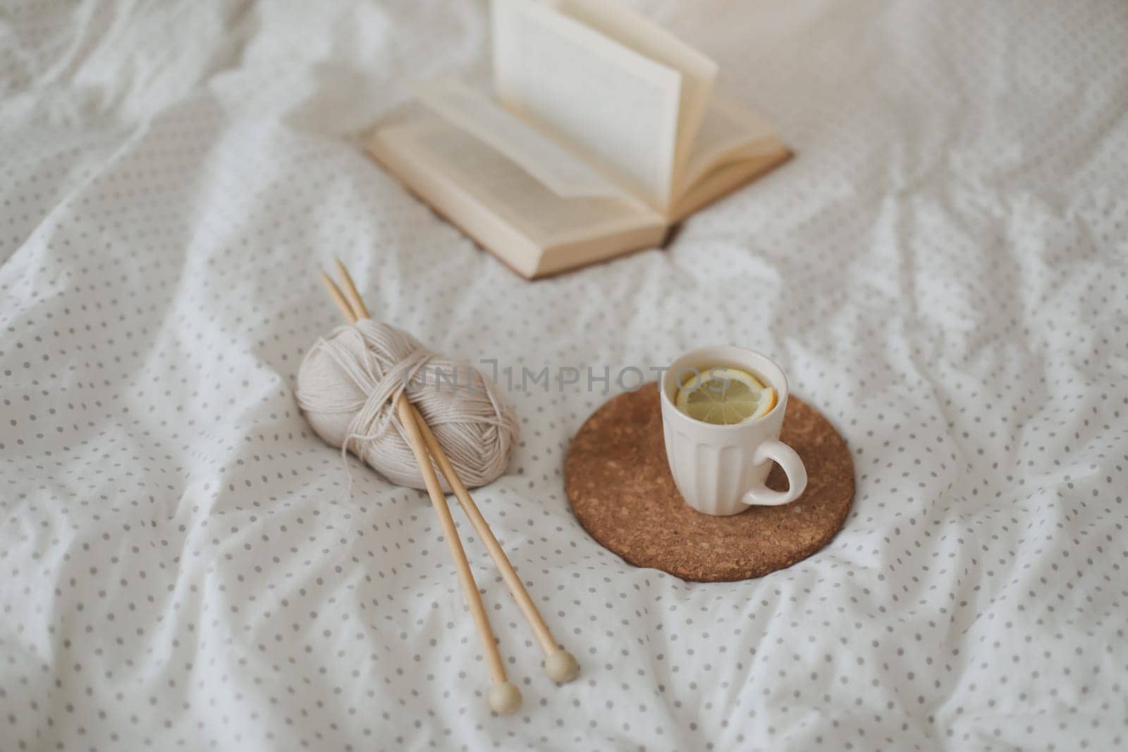 Cozy morning still life with a cup, candle, needles and a woolen yarn in white bed. Knitting warm woolen sweater or scarf top view. Hygge lifestyle, cozy mood. Handicraft day concept. by paralisart