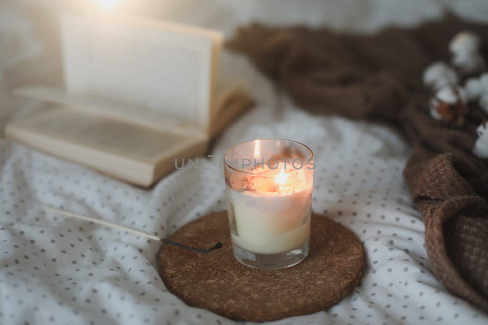 Cozy still life interior details with a book, candle and a cotton twig in warm soft bed. Sweet home by paralisart
