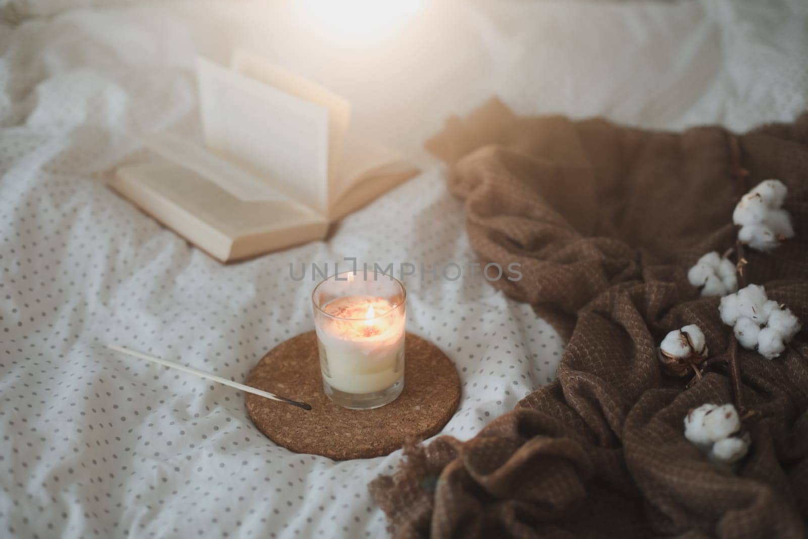 Cozy still life interior details with a book, candle and a cotton flower in warm soft bed. Sweet home