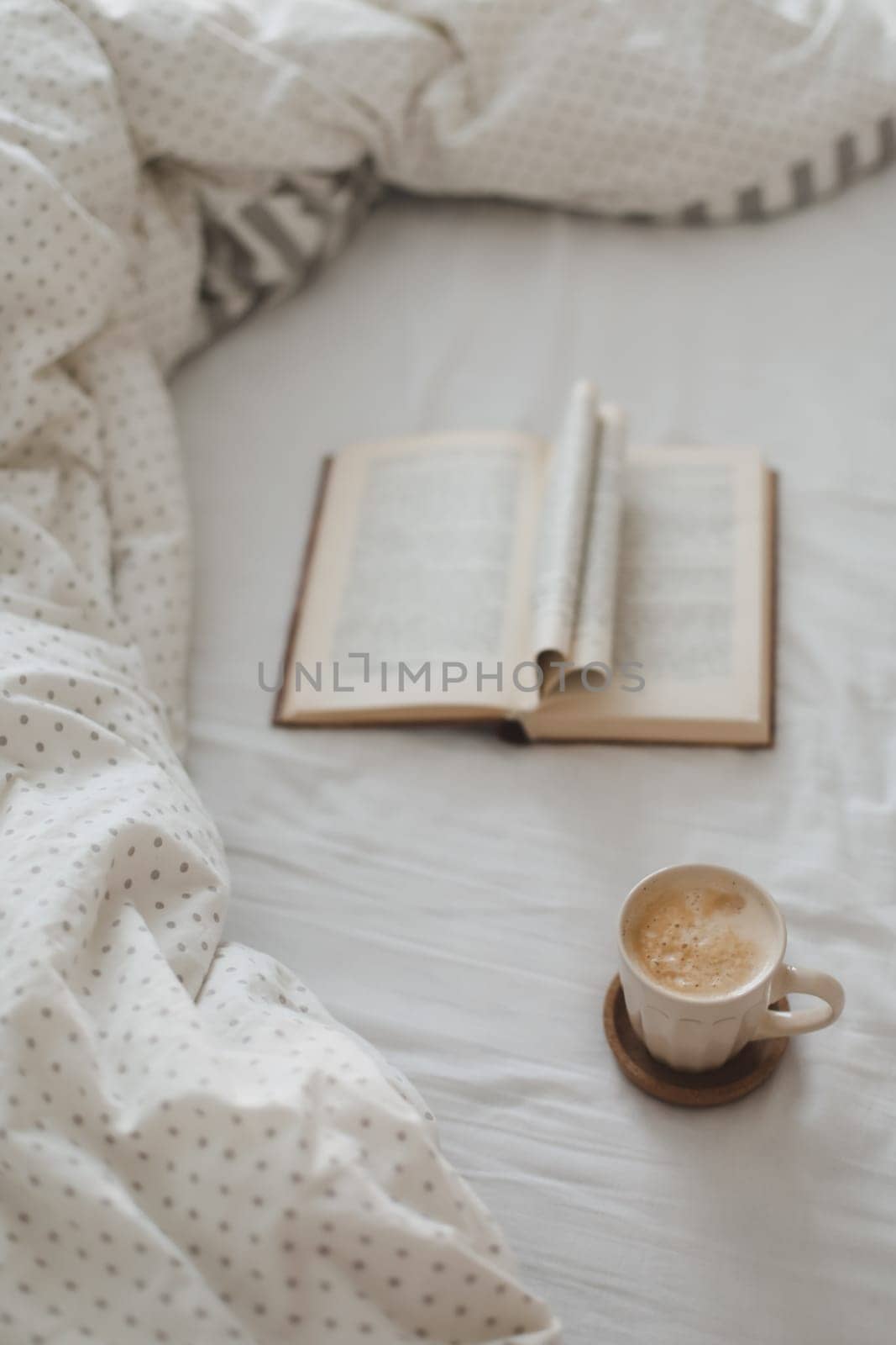 Cozy morning composition with a coffee cup and a book with pages folded into a heart shape in bed.