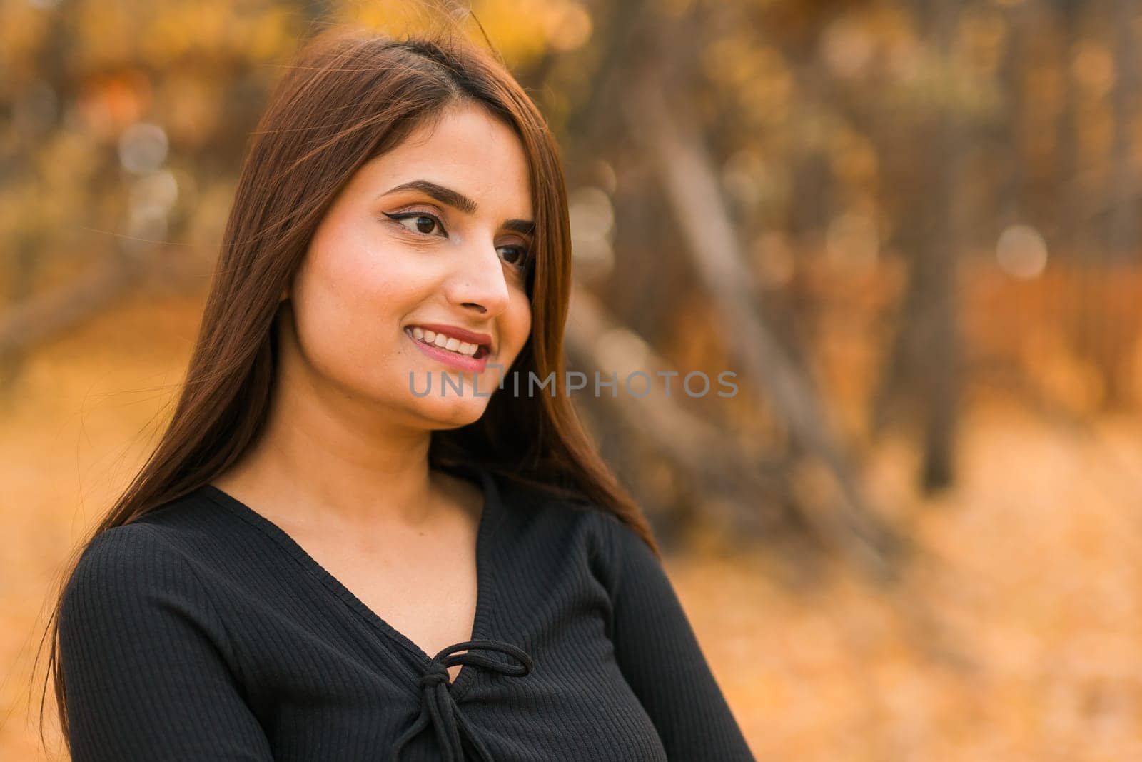 Close-up portrait of a young beautiful confident Indian Asian woman in fall outdoor. Happy and natural smiling female. Generation z and gen z youth