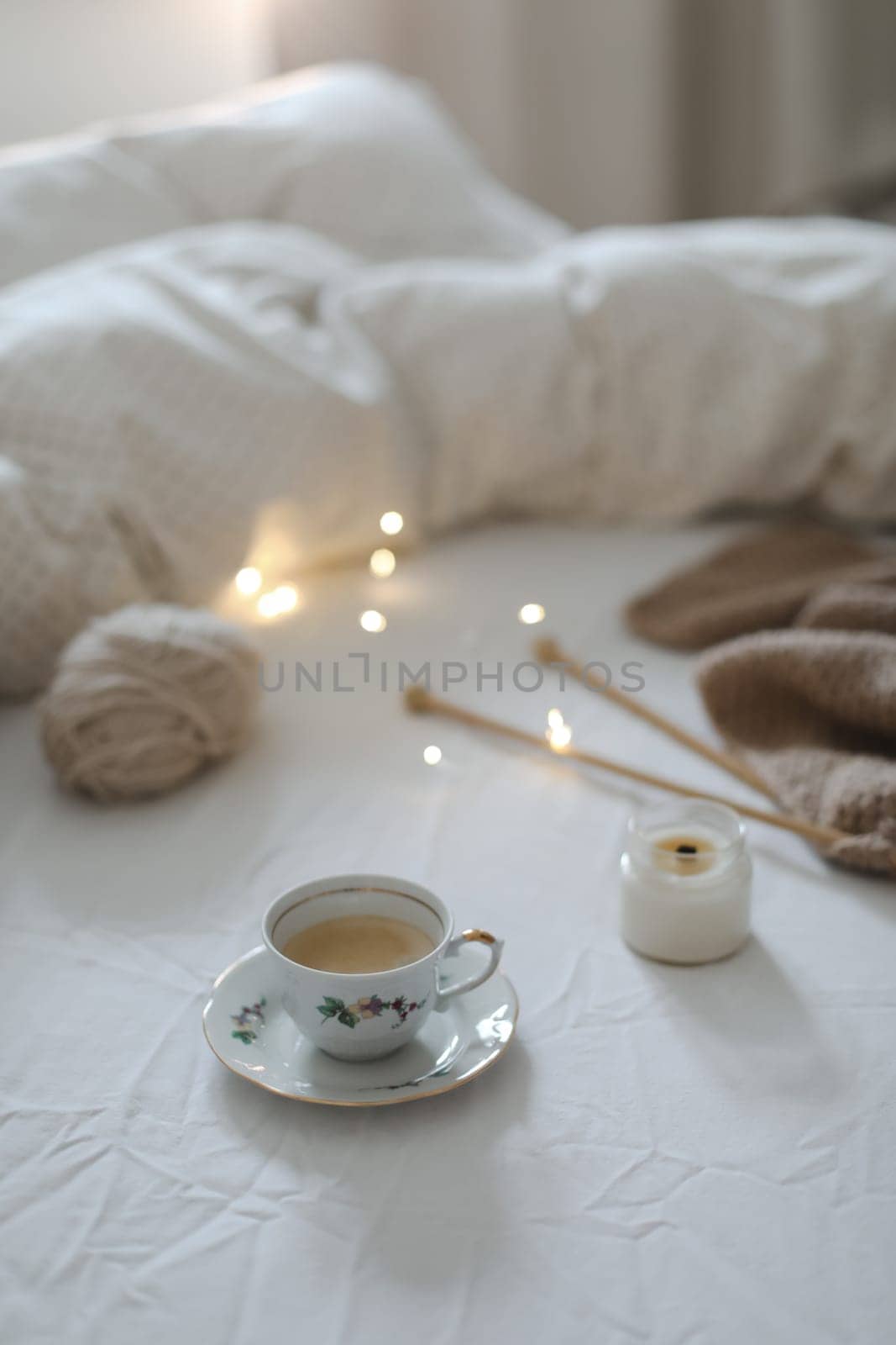 Cozy morning still life with a coffee cup, candle, needles and a woolen yarn in white bed. Knitting warm woolen sweater or scarf top view. Hygge lifestyle, cozy mood. Handicraft day concept. by paralisart