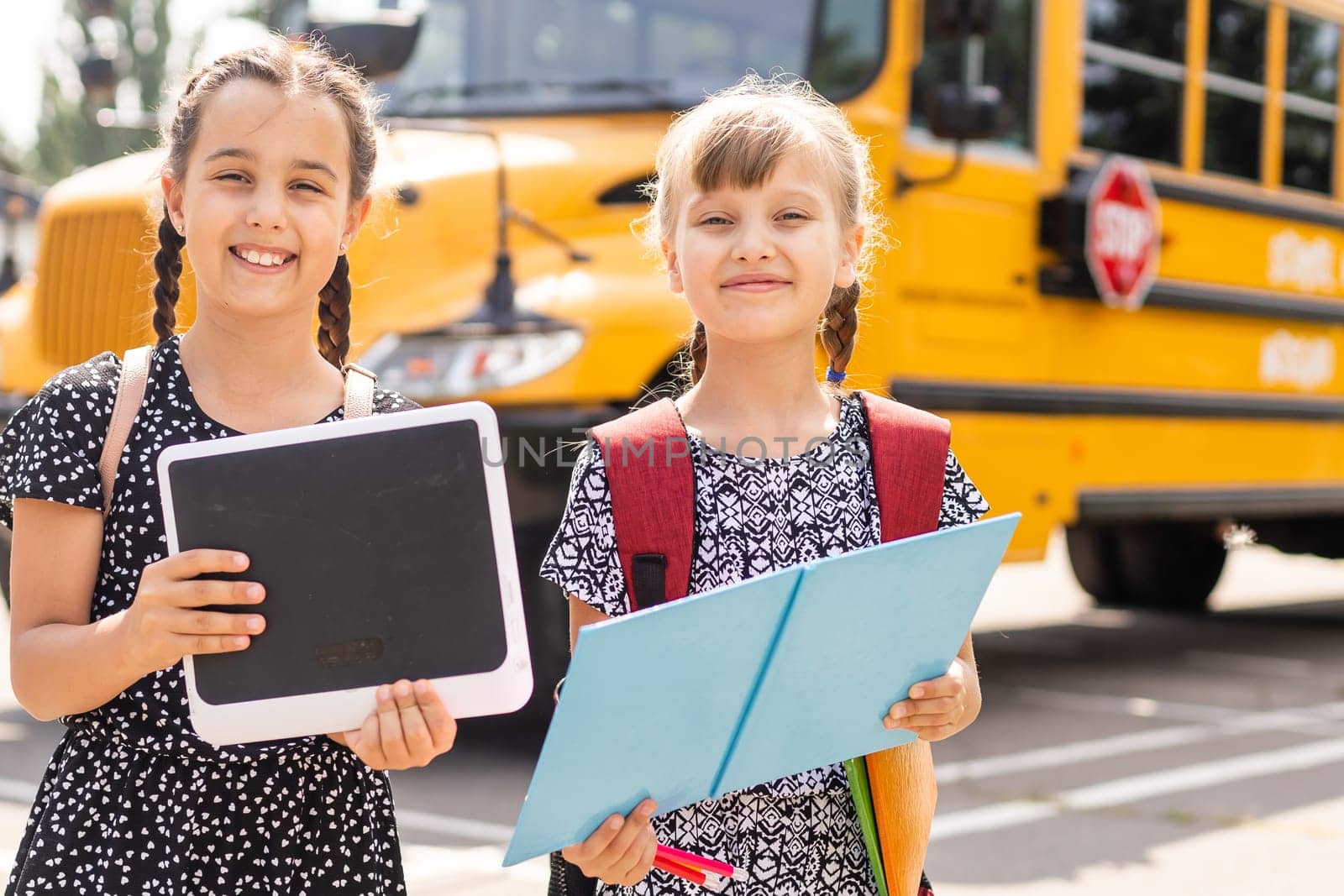 Cheerful little girls next to school bus. Backback. Back to school concept