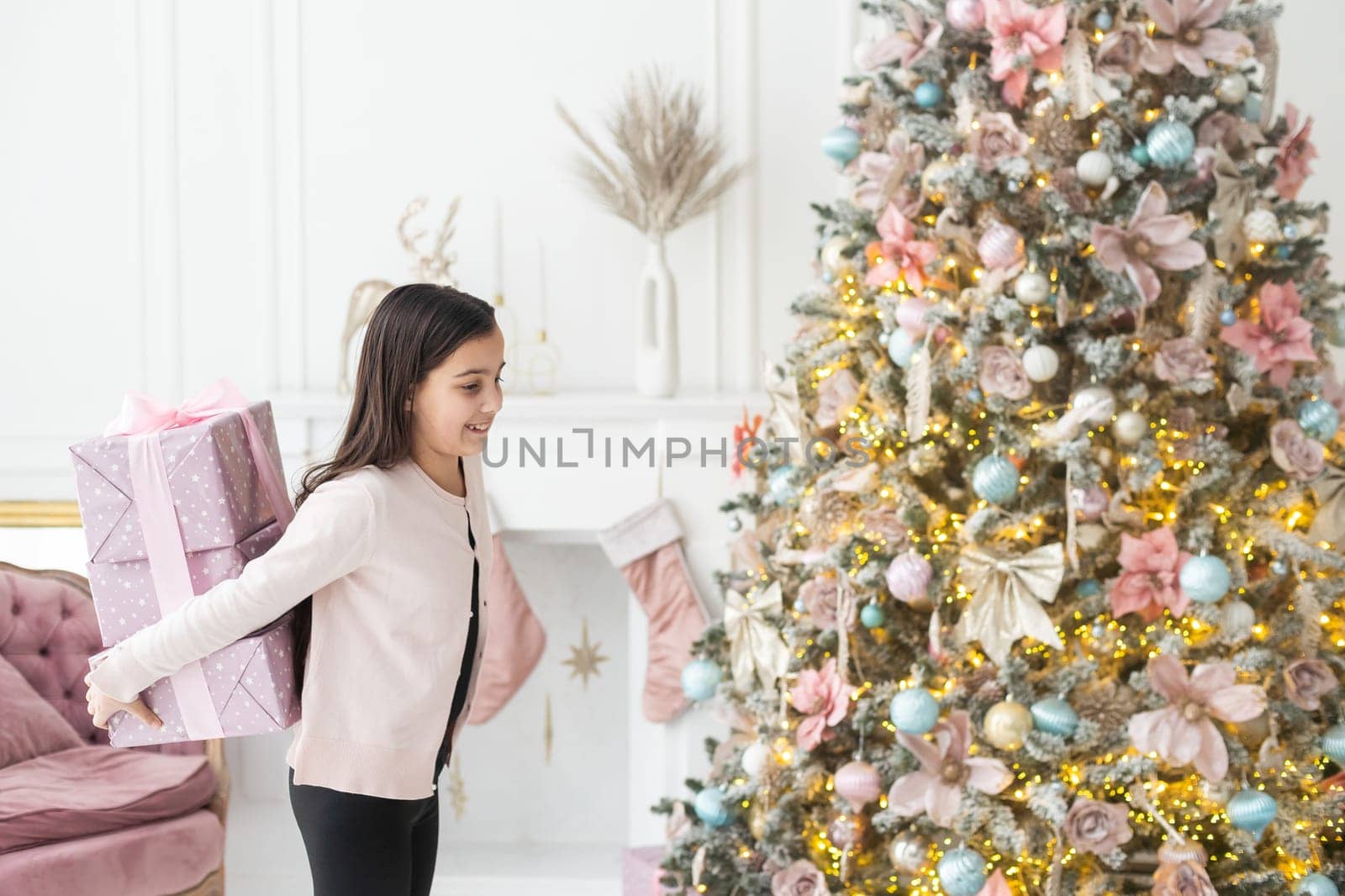 A very beautiful cute girl holding a gift in her hands. Christmas mood. The child gives a present happy smiling. Place for text. Bokeh garlands. new Year.