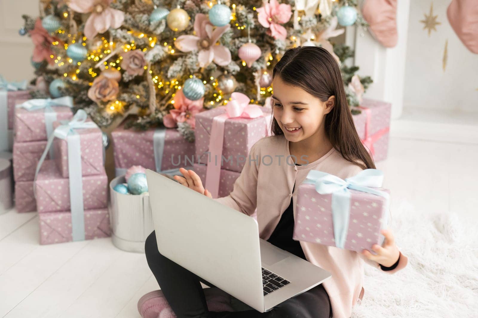 teenage girl works at home remotely with laptop on the background of a Christmas tree. Quarantine, work on holidays. atmosphere and work at home by Andelov13
