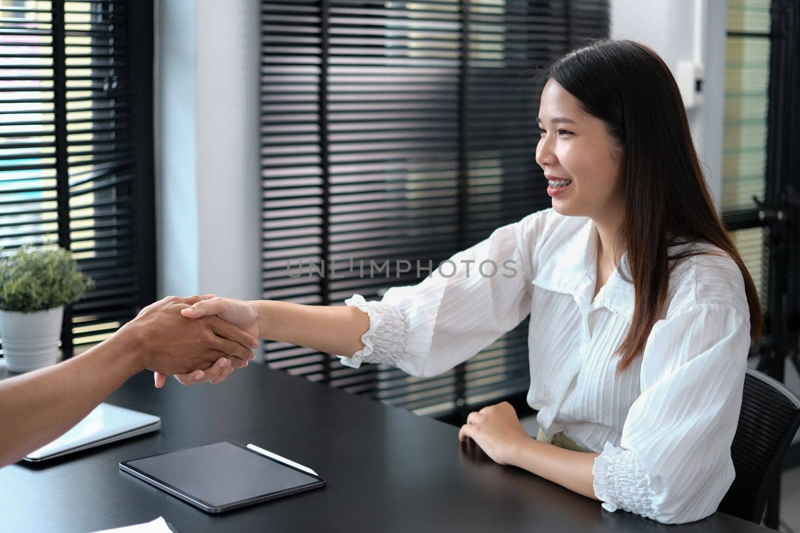 Smiling Asian female recruitment manager shaking hands with a job applicant after interview..