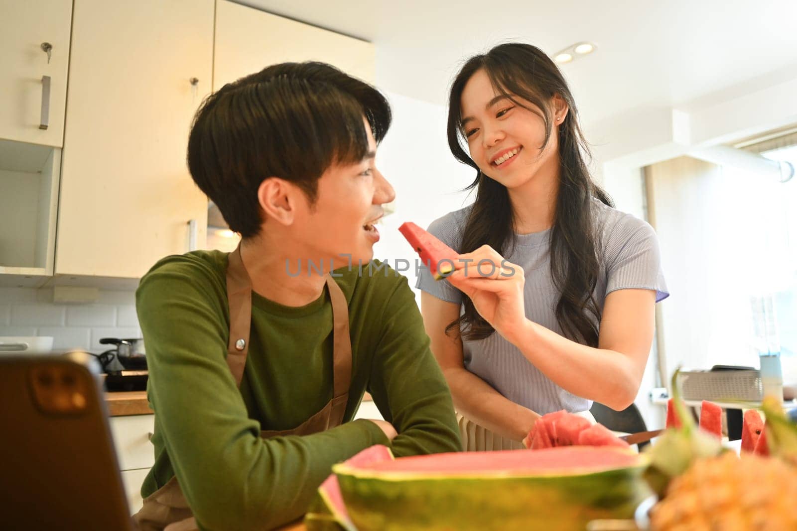 Happy young asian couple in home kitchen eating slice of fresh watermelon. Freshness, diet and healthy eating concept.