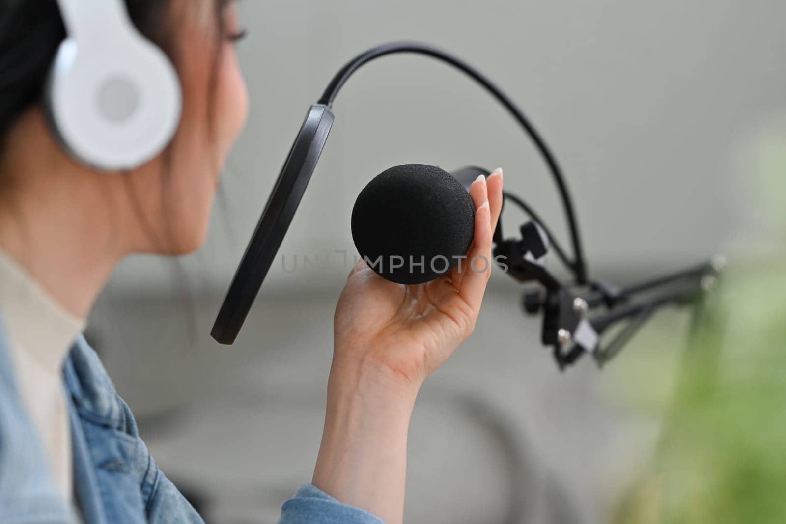 Side view of woman content creator in headphone talking through microphone for recording conversation for channel.