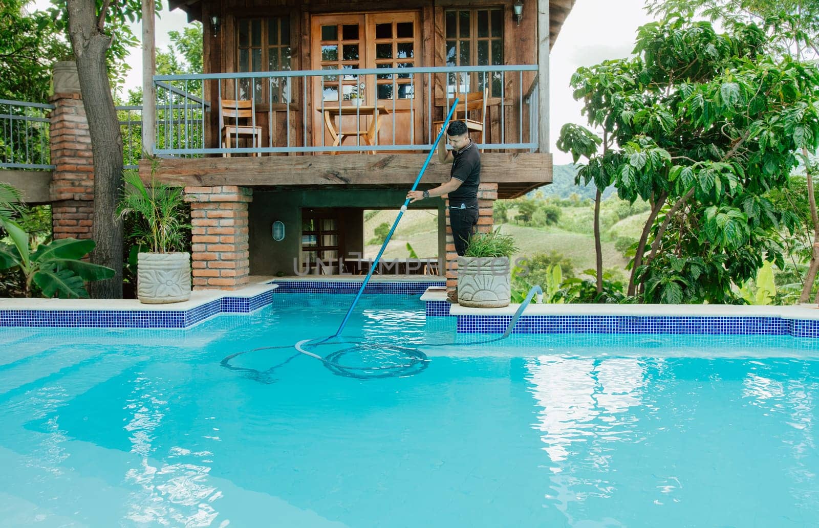 Maintenance man cleaning swimming pool with vacuum suction hose. Worker cleaning a beautiful swimming pool with suction hose