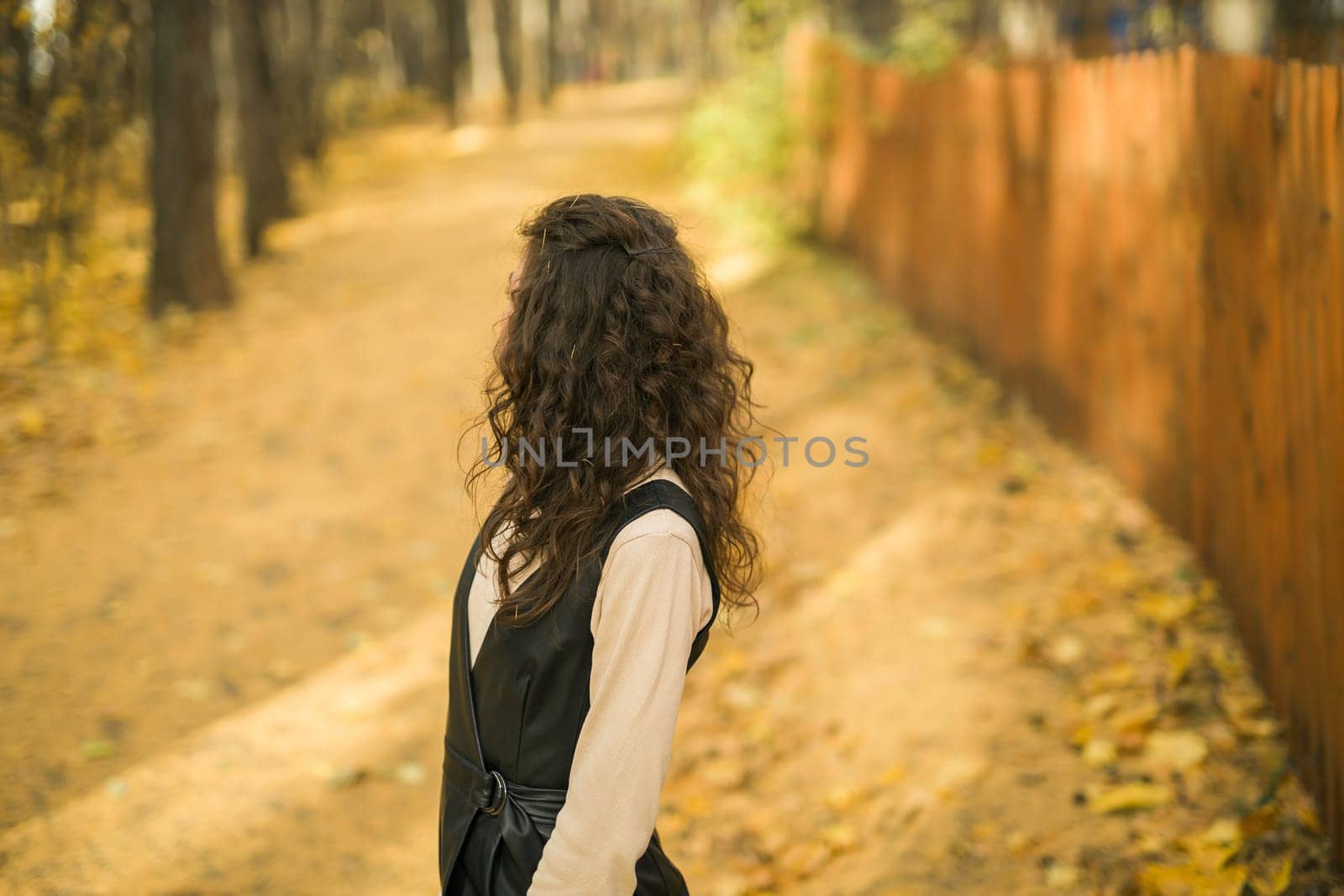 Girl in fall park back view copy space. Woman with long curly hair. Beautiful sunlight in forest. Hair care. Millennial Generation and youth. by Satura86