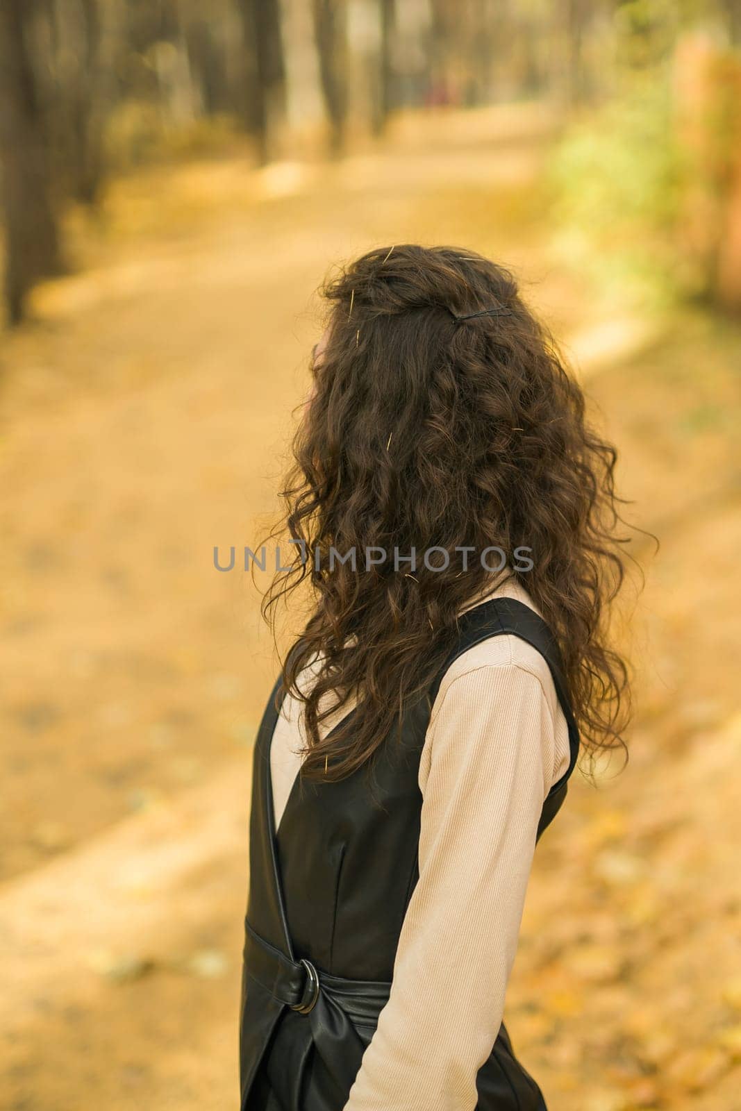 Girl in fall forest. Woman with long curly hair. Beautiful sunlight in the forest. Hair care. Millennial Generation and youth