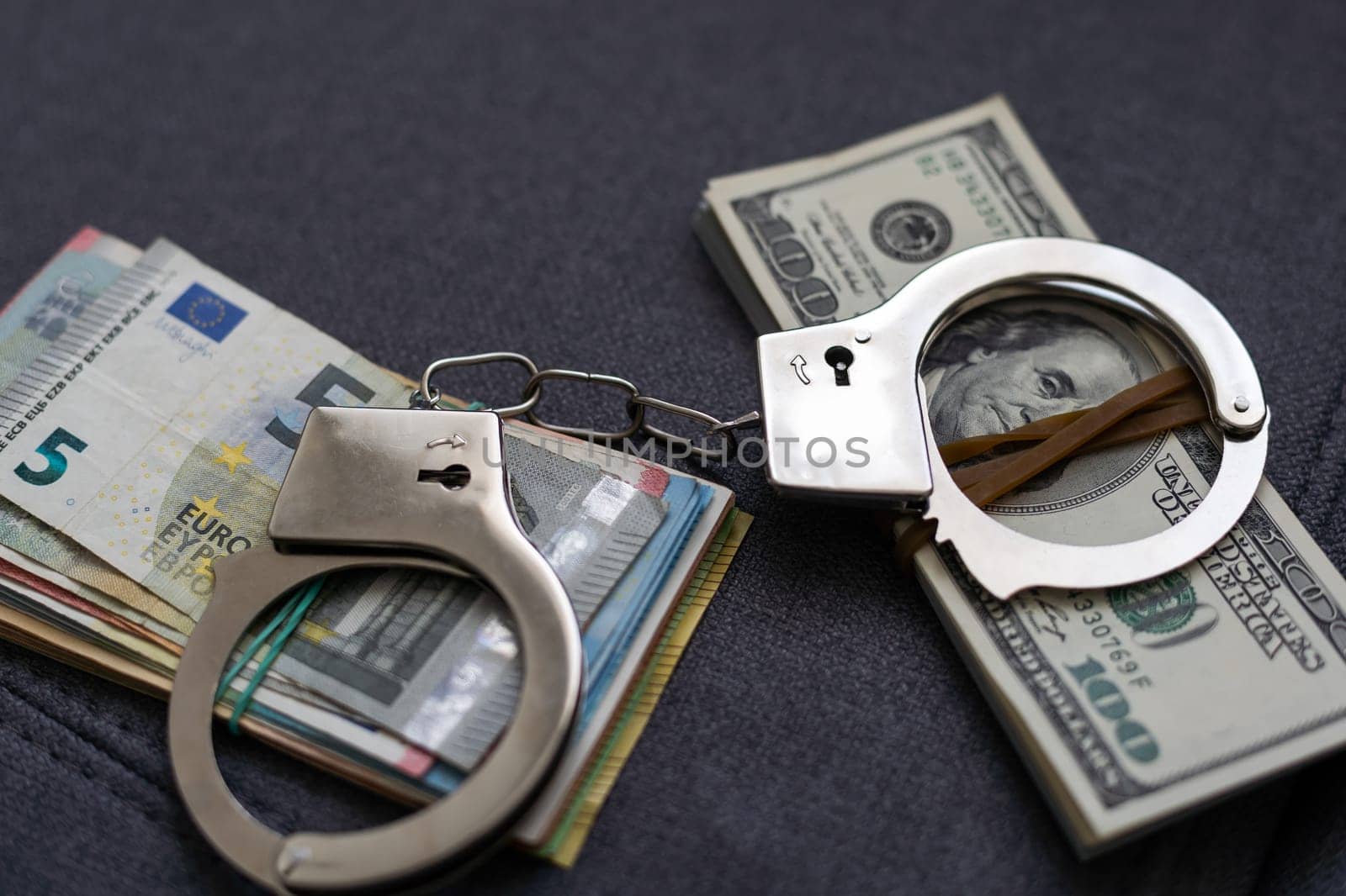 Police handcuffs lie on many dollar bills isolated on black background. Crime. justice and money. Concept of crime and corruption with handcuffs. by Andelov13