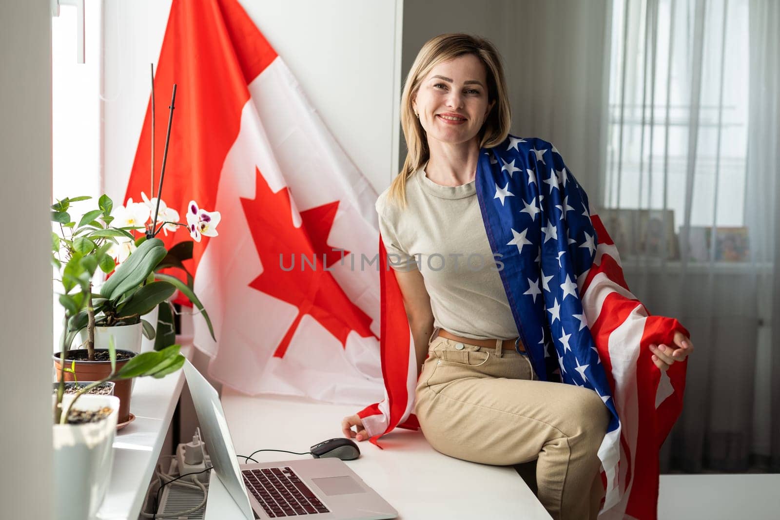 Portrait of happy young woman with USA flag learning American English online from home using laptop. Smiling female student sitting at table and taking online educational course in foreign languages. by Andelov13