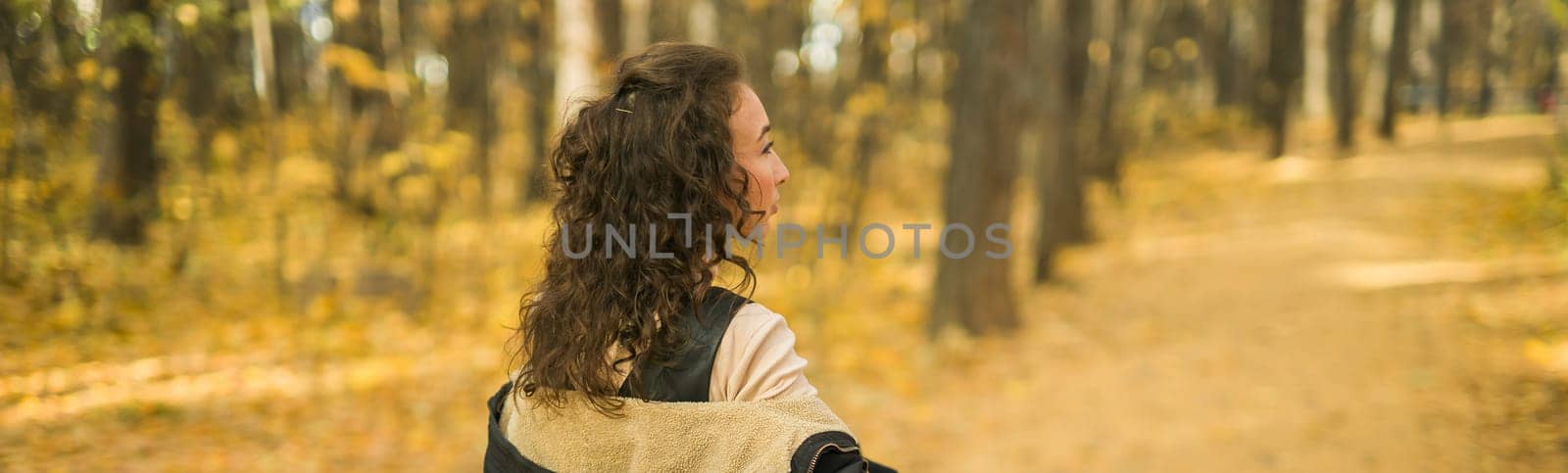 Banner autumn portrait of a beautiful happy curly woman in fall season copy space mockup. Millennial generation female. Natural beauty concept. Rear view by Satura86