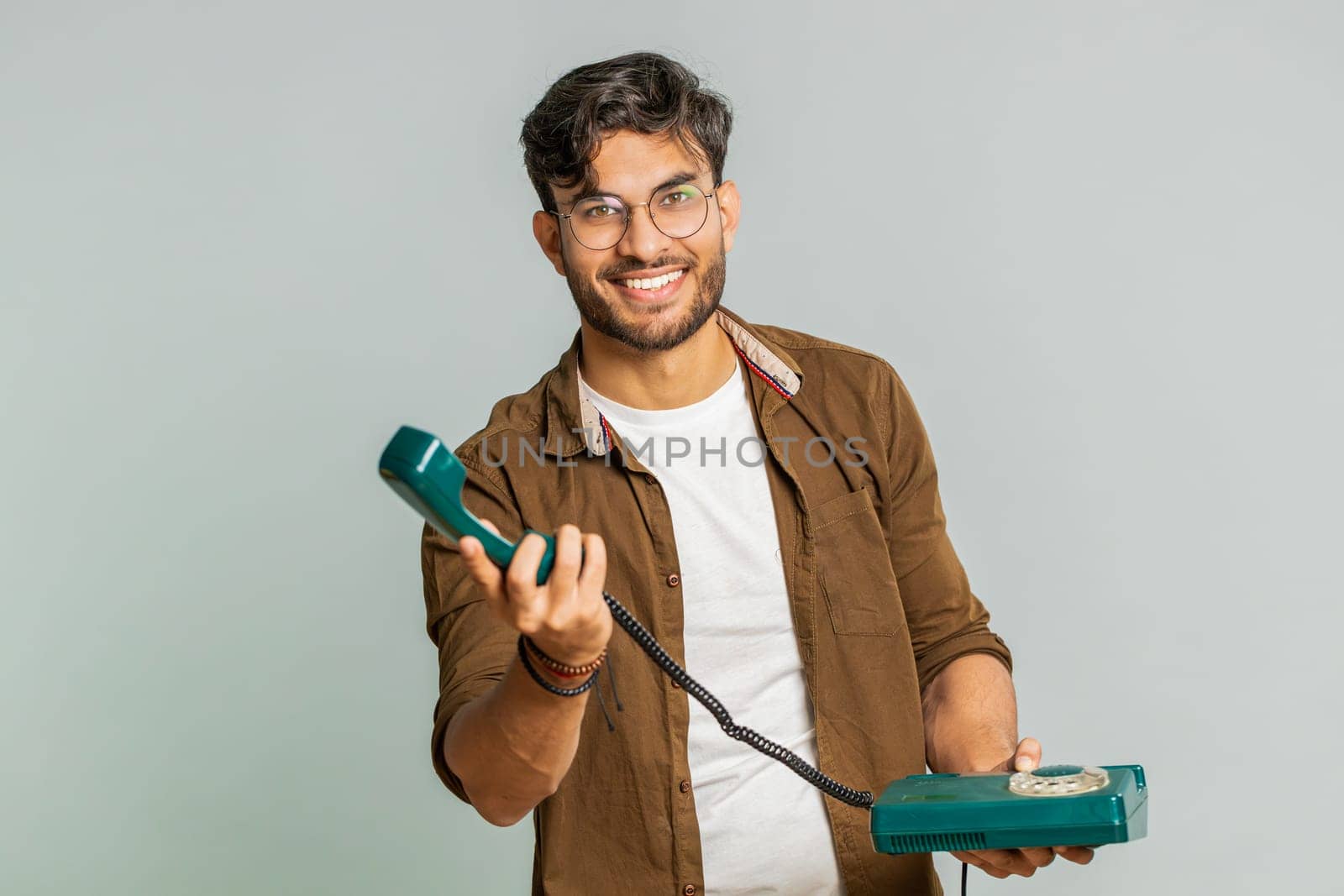 Hey you, call me back. Indian young man talking on wired landline vintage telephone of 80s, advertising proposition of conversation, online shopping, hotline. Arabian guy isolated on gray background