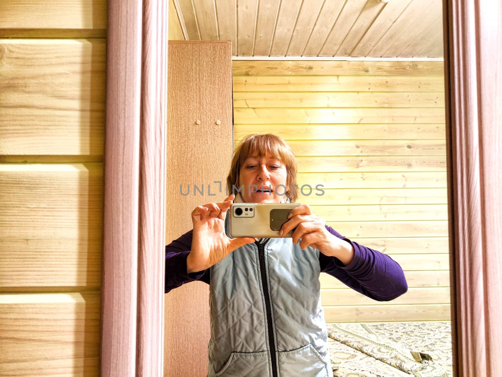 Middle-aged woman using smartphone for selfie and blogging. Female blogger poses in a photo. The girl admires herself in the mirror