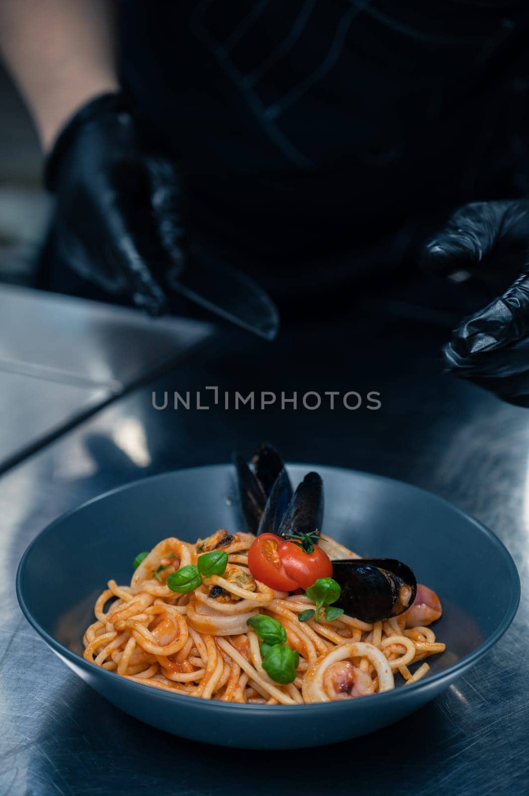 Chef preparing Seafood Pasta with mussels with basil and tomato in black plate