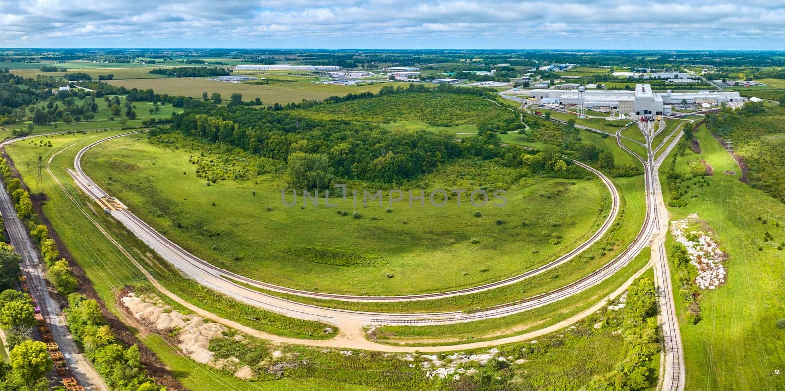 Image of Panorama railroad tracks Progress Rail Services aerial with lush grass and trees, sunny summer day