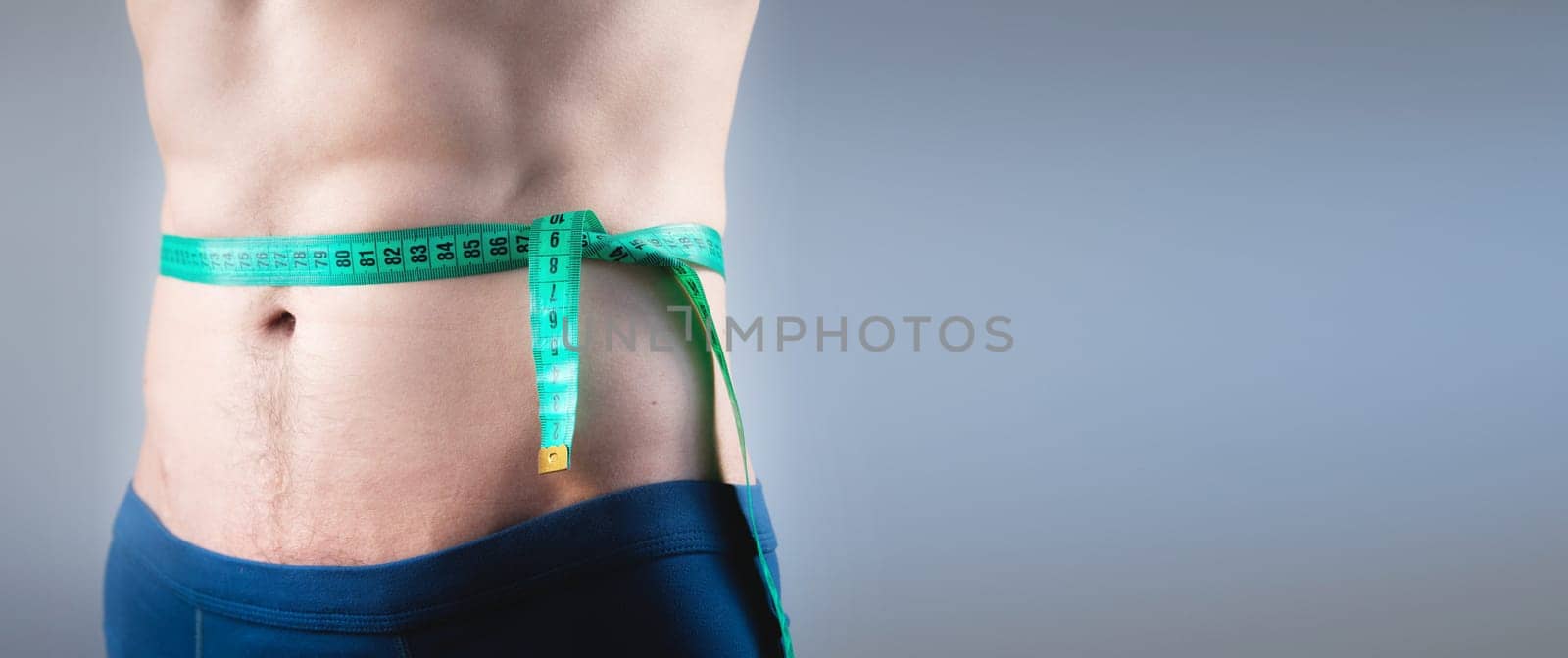 Close-up of an athlete measuring body fat with a centimeter on a gray background. A man lost weight thanks to a diet and pumped up his abs, photo for banner by yanik88