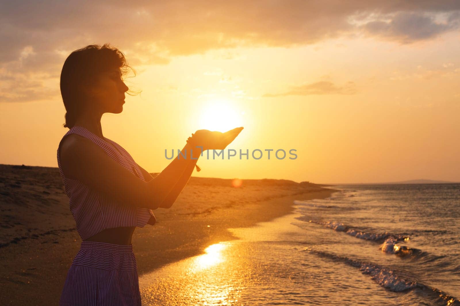 Portrait of a young woman in the form of a silhouette and hands holding the sun. Sunset over the sea, the sun on the palms of a calm girl.
