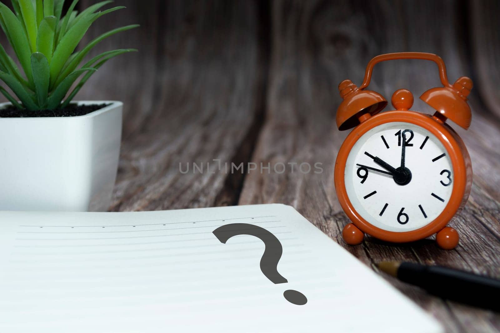 Question mark on notepad alarm clock on wooden background. Q and A concept.