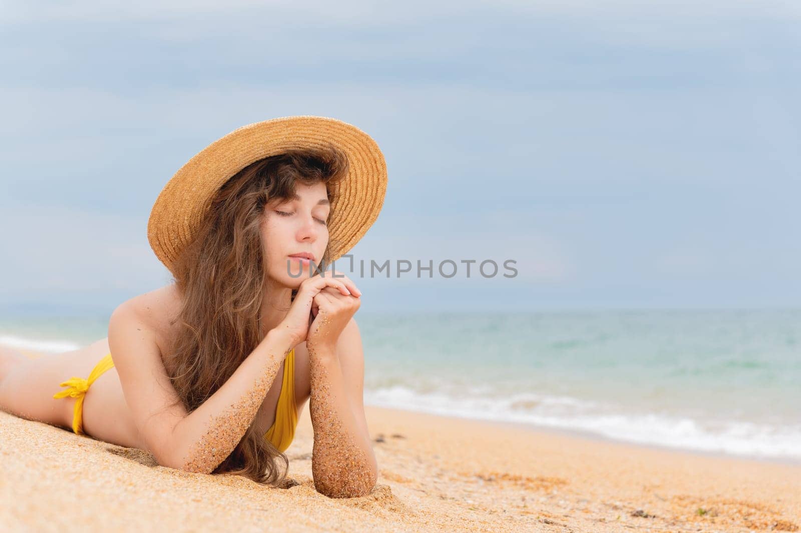 Summer lifestyle. Portrait of a beautiful girl with a slim body in a bikini enjoying life and lying with her eyes closed on the sand on the beach of a tropical island. Vacation by yanik88