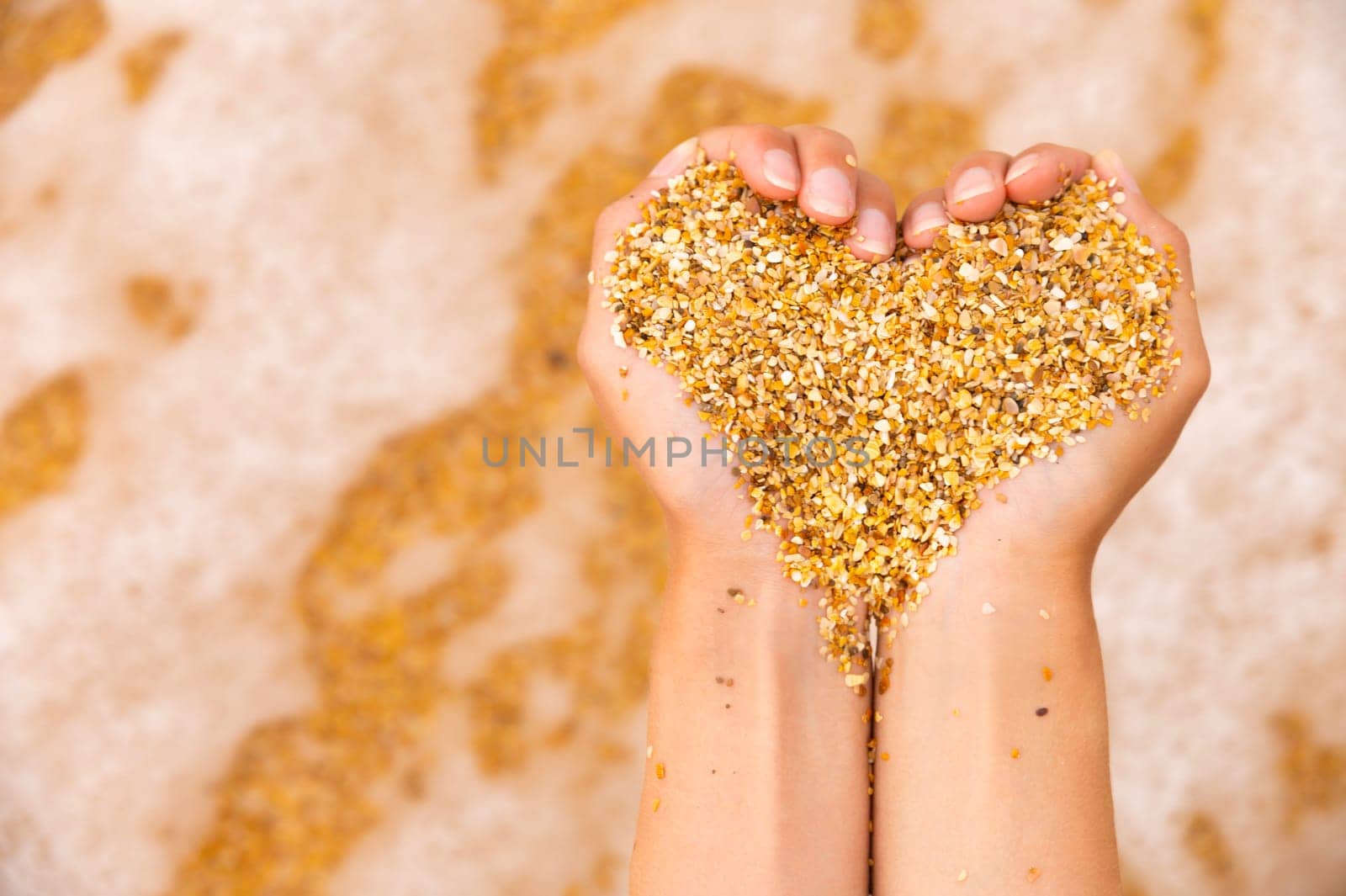 Soft heart shapes of women's hands over the beach. Women's hands hold sand in the shape of a heart against the background of sea waves.