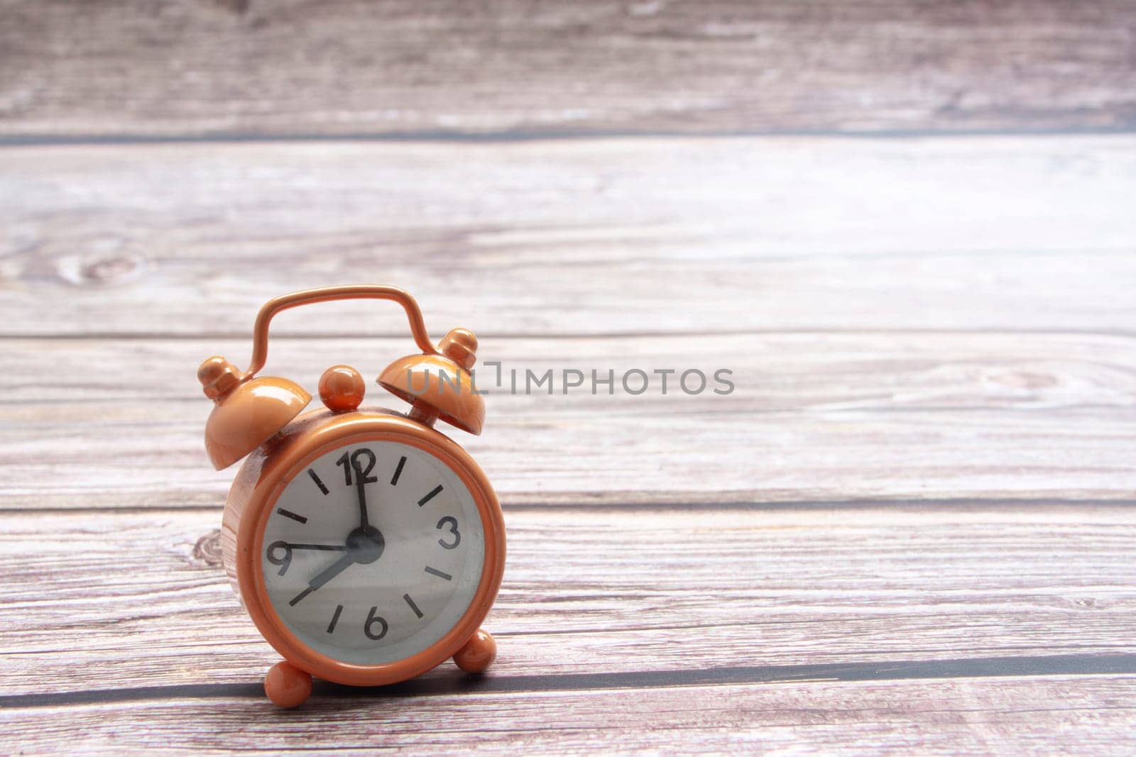 Orange alarm clock isolated on wooden desk. The clock set at 8 o'clock. Copy space.