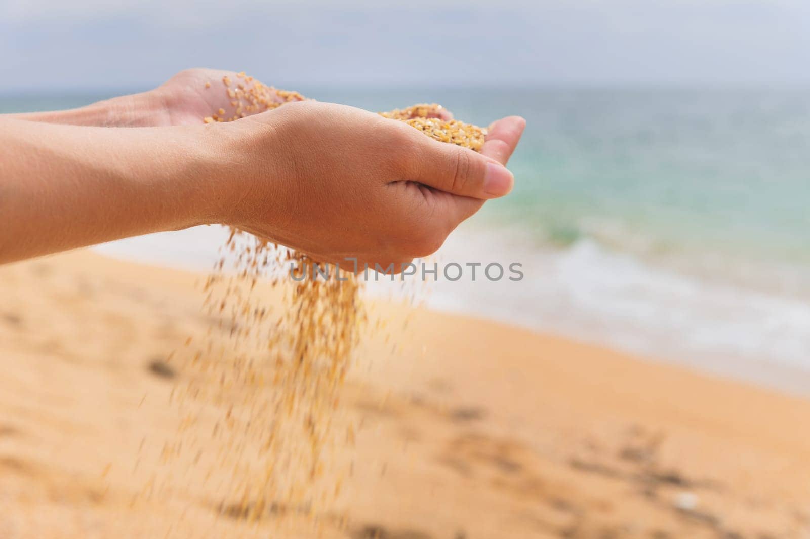 The hand releases the falling sand. Golden sand flows through your fingers on a sea background. Summer beach holiday and time passing concept.