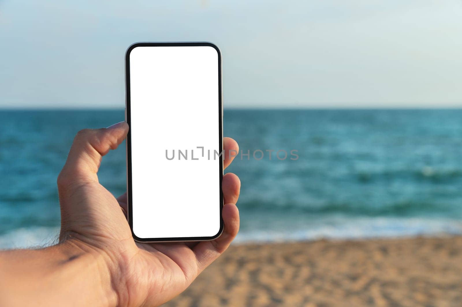 Hand holding smartphone on the beach, mobile mockup of blank screen, Take your screen to put on advertising. Summer vacation concept by yanik88