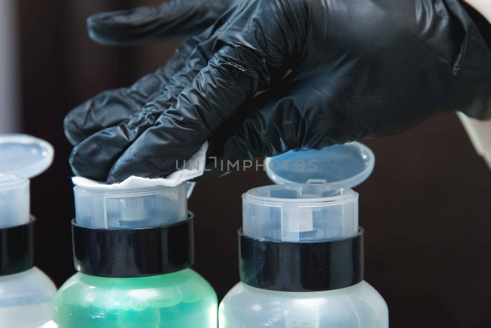 Close-up of a man holding a cotton pad and liquid cosmetics for makeup removal. beauty salon, a master in black special gloves prepares the workplace.