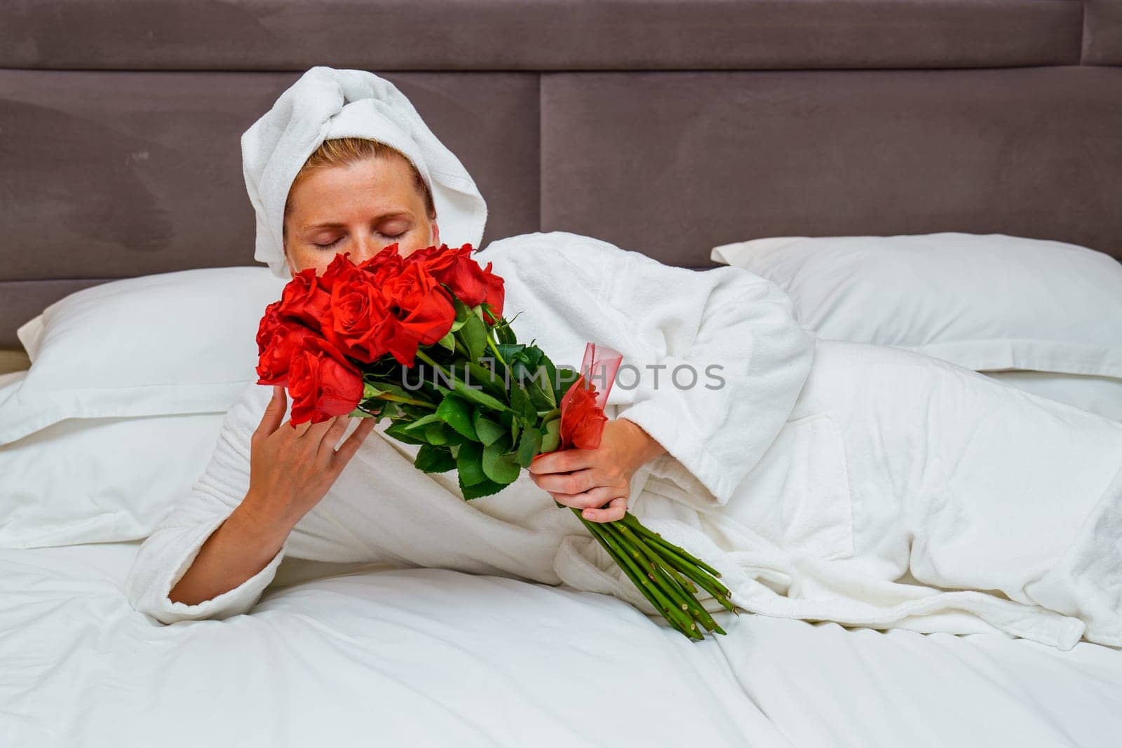 Tranquil romance: Gorgeous woman with a large bouquet of red roses resting on a hotel bed by PhotoTime