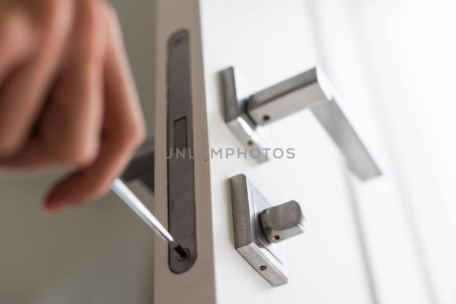 A locksmith is repairing an interior door lock. Close-up of male hands repairing or replacing an entrance door lock with a hex screwdriver by Andelov13