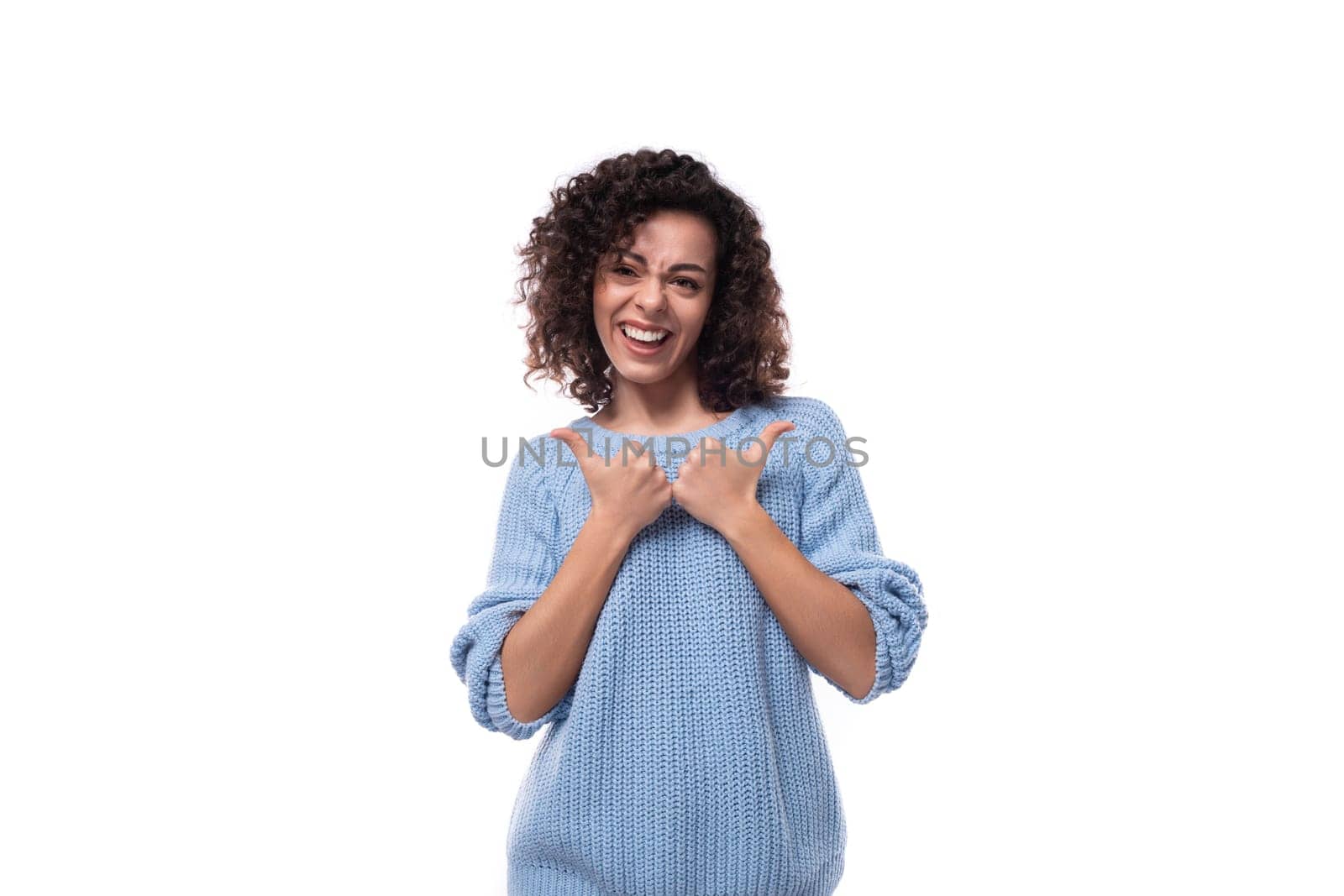 a young caucasian woman with curly natural dark hair is dressed in a casual warm blue jacket actively gesturing with her hands by TRMK