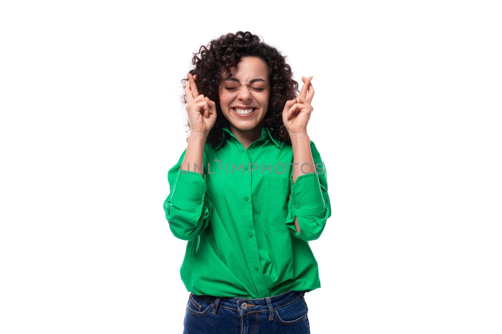 young stylish caucasian brunette woman with curled hair dressed in a green shirt crossed her fingers in anticipation.