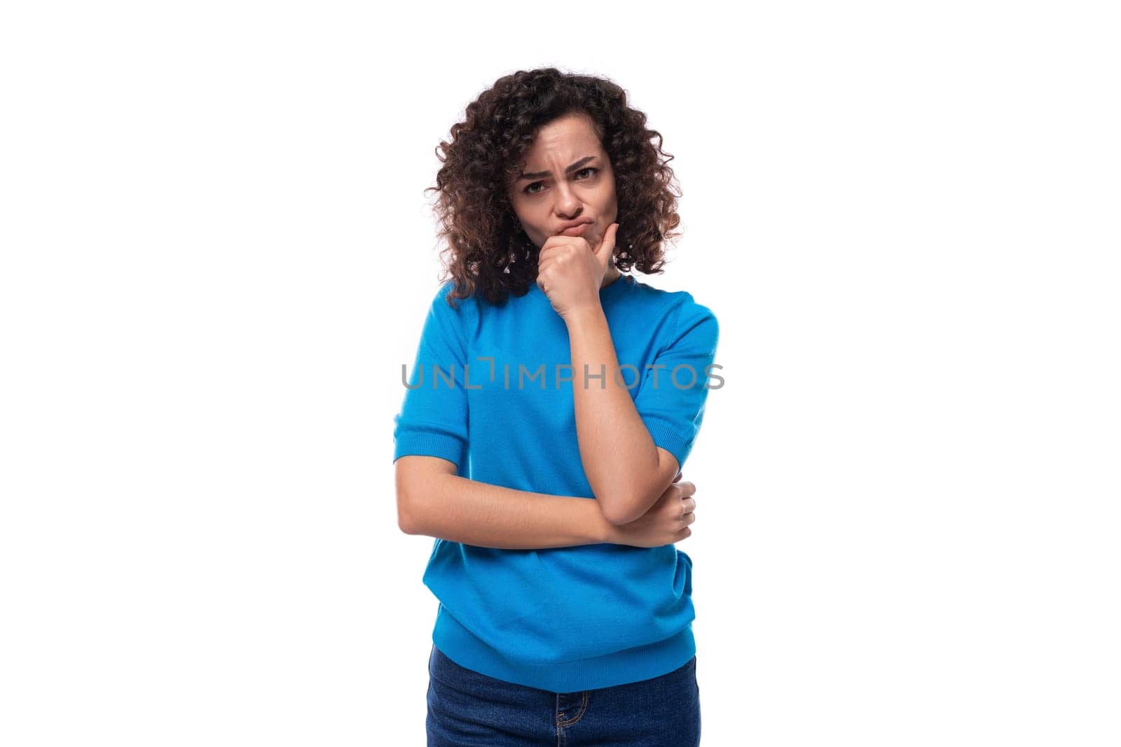 young brunette lady with curly hair dressed in a blue jacket stands thoughtfully.