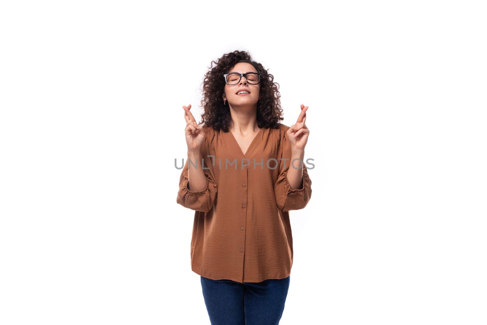 young smart slim woman with curly haircut dressed in brown blouse crossed her fingers by TRMK