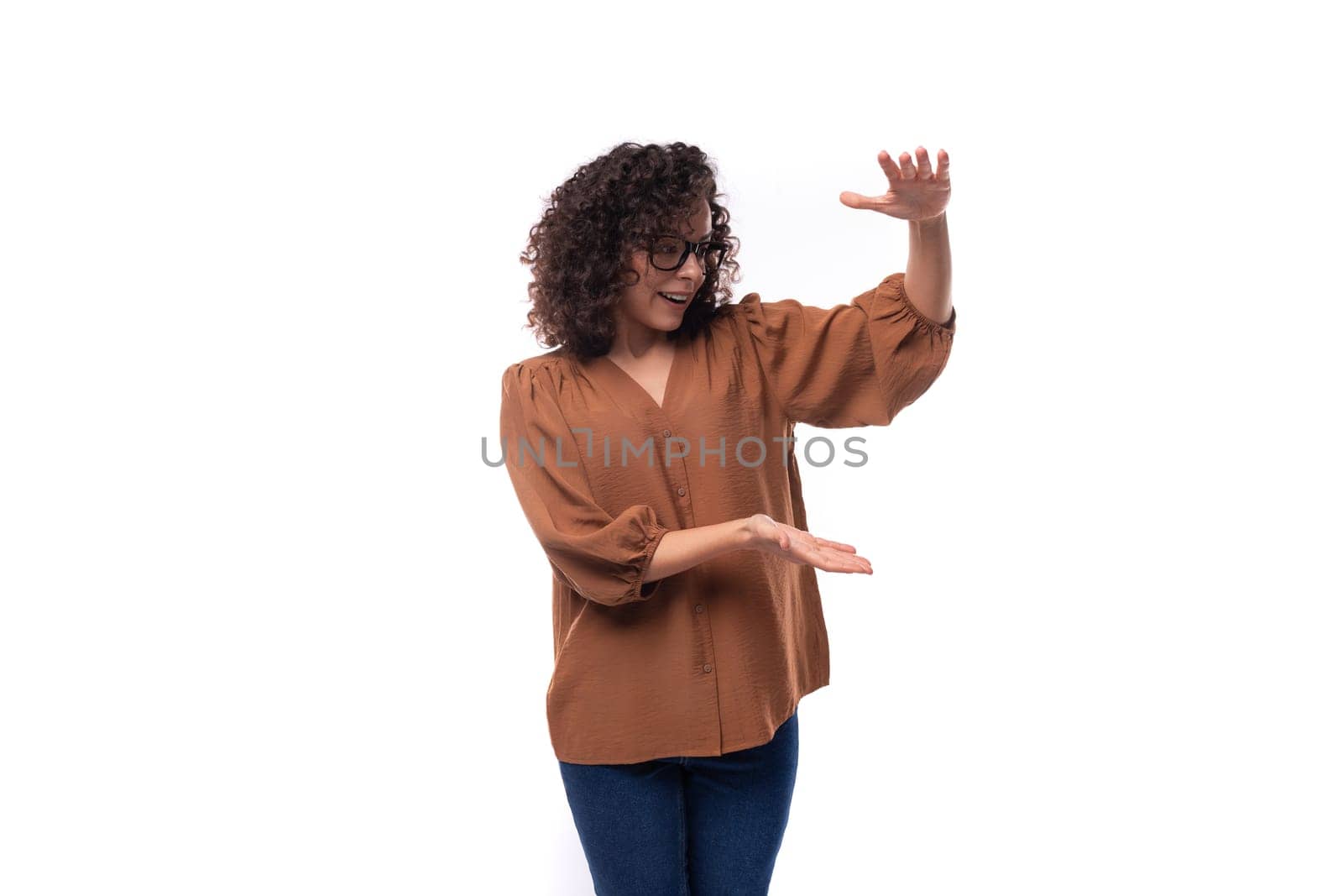 young well-groomed caucasian woman with curly black hair dressed in a brown blouse actively gesticulates.