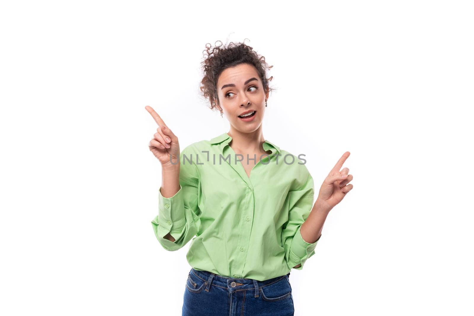 stylish young brunette curly woman with ponytail dressed in a green shirt points fingers towards advertising by TRMK