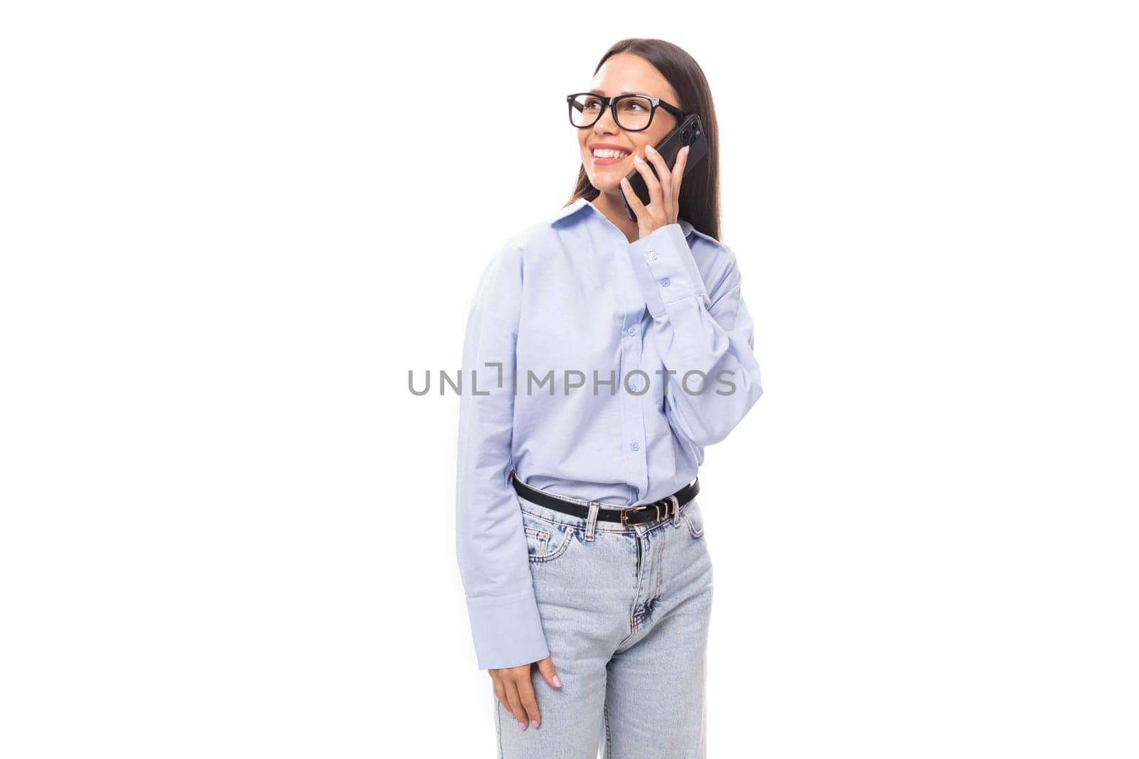 pretty young brunette european woman dressed in a blue shirt uses a smartphone to chat in social networks on an isolated background with copy space.