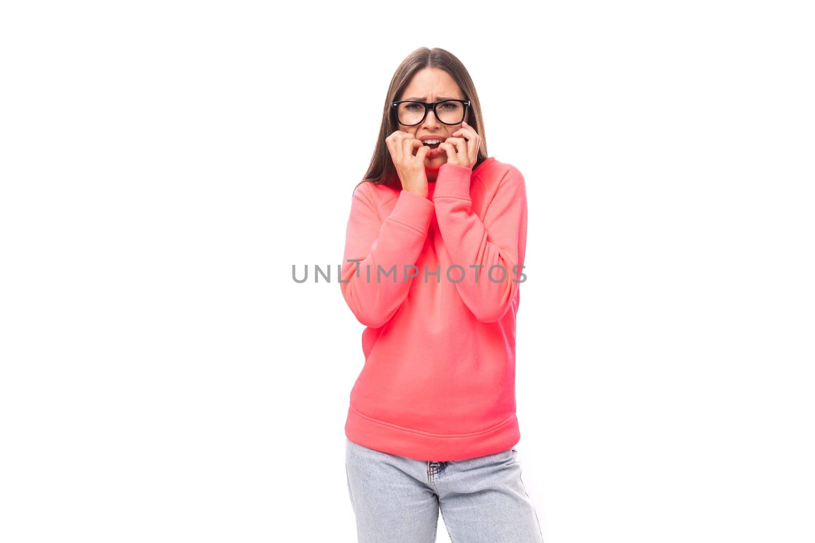 portrait of a young positively energetic european model woman with long black hair dressed in a pink sweater on a white background with copy space.